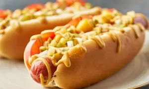 Dwa apetyczne hot dogi z Żabki, polane musztardą, z dodatkiem pomidorów i ogórków. Zastanawiasz się, ile kcal ma hot dog z Żabki?