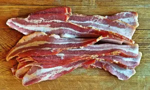 Słoneczny boczek, idealny na śniadanie. Zastanawiasz się nad boczek kcal? Oto porcja pysznego, surowego boczku na drewnianej desce.