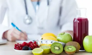 Lekarz pisze zalecenia dietetyczne. Na stole owoce i sok, które mogą być produktami zakazanymi przy uchyłkach.
