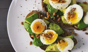 Tosty z awokado i jajkiem na miękko, posypane orzeszkami pinii i pieprzem. Idealne na śniadanie w ramach dieta 1200 kcal.