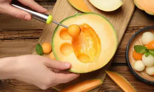 Ręka formuje kulki z melona, który ma niski melon indeks glikemiczny. Obok leżą kawałki melona i miseczka z owocowymi kulkami.