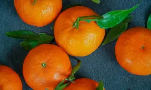 Kilka soczystych mandarynek z zielonymi listkami na ciemnym tle. Idealne na zdrową przekąskę, bo mandarynka kcal jest niska.