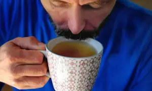 Mężczyzna w niebieskim swetrze pije napar z ziół na refluks z ozdobnego kubka.