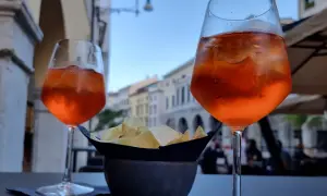 Dwa drinki Aperol Spritz i miseczka chipsów na stoliku. Czy alkohol podnosi cholesterol? To pytanie zadaje sobie wielu, popijając orzeźwiający drink.