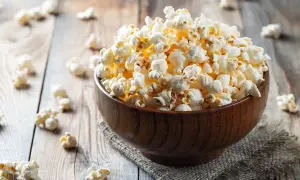 Drewniana miska pełna karmelowego popcornu na drewnianym tle.