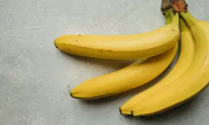 Trzy żółte banany leżą na szarym tle. Jeden banan kcal to zdrowa przekąska.