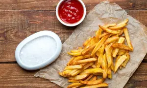 Złociste, chrupiące średnie frytki McDonald's na papierze, obok miseczki ketchupu i soli. Ile kcal mają te pyszności?