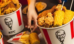 Wiadro KFC z kurczakiem, frytkami i kolbami kukurydzy.