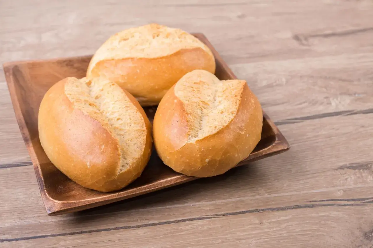 Trzy świeże bułki pszenne na drewnianej desce. Zastanawiasz się nad ich kcal?