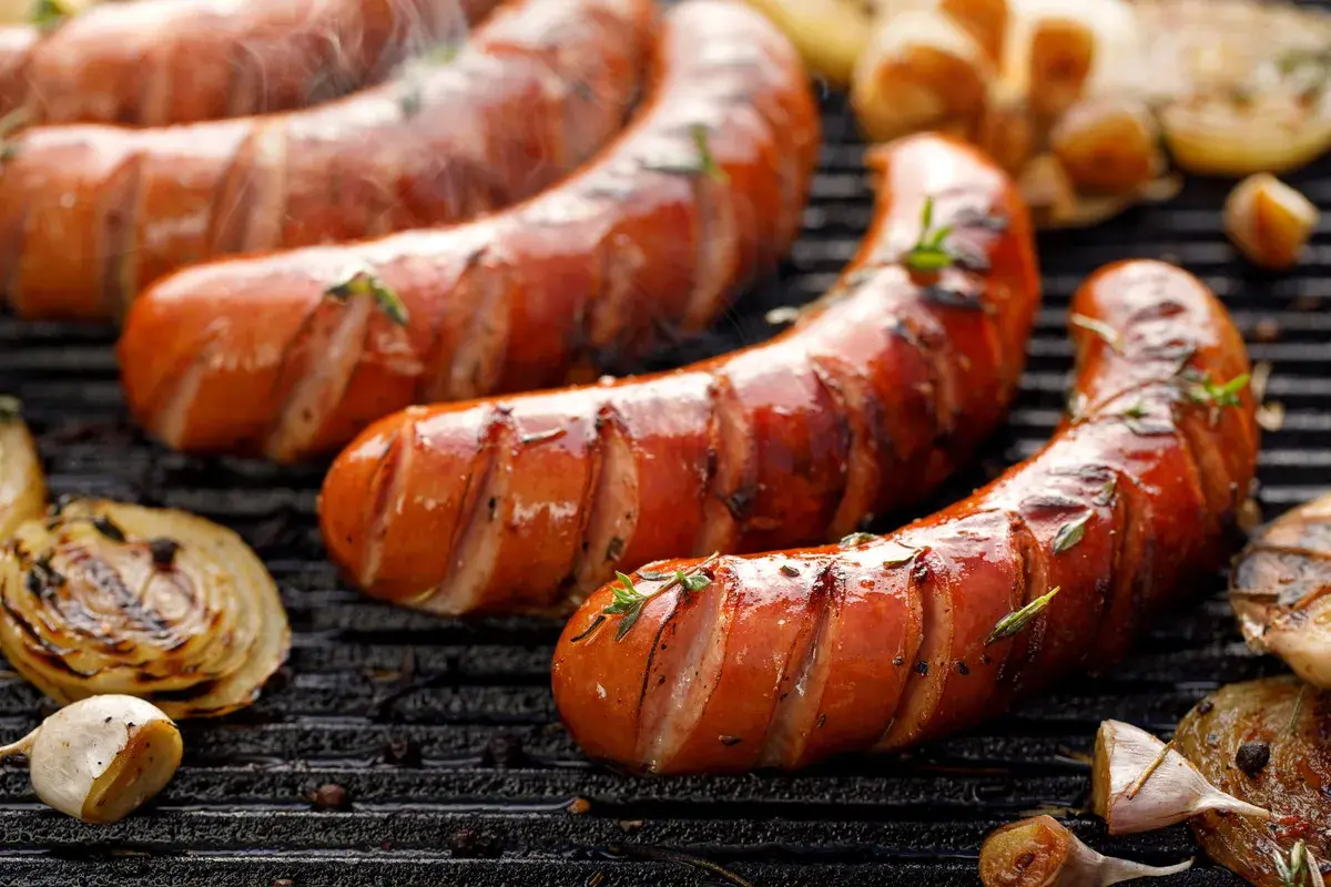 Soczysta kiełbasa śląska z grilla, parująca i pachnąca. Obok grillowana cebula i czosnek. Idealna na letnie wieczory, choć warto sprawdzić kiełbasa śląska kcal.