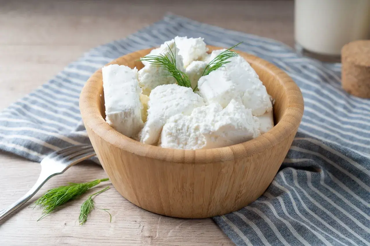 Półmisek z twarogiem półtłustym, udekorowany koperkiem. Obok widelec i szklanka mleka. Idealny na lekki posiłek, z niską zawartością kcal.