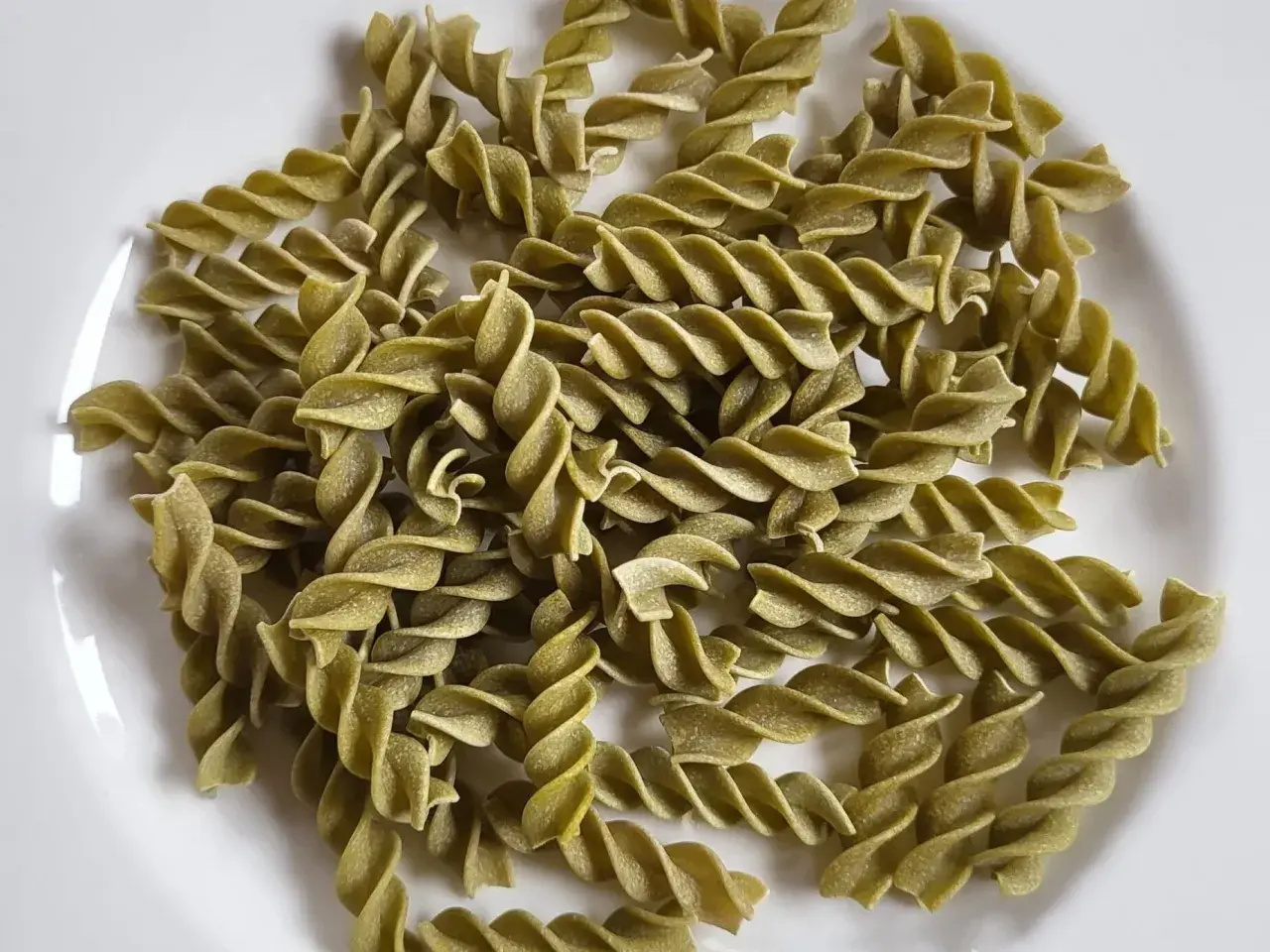 Zielone fusilli, czyli makaron z zielonego groszku, ułożone na białym talerzu.