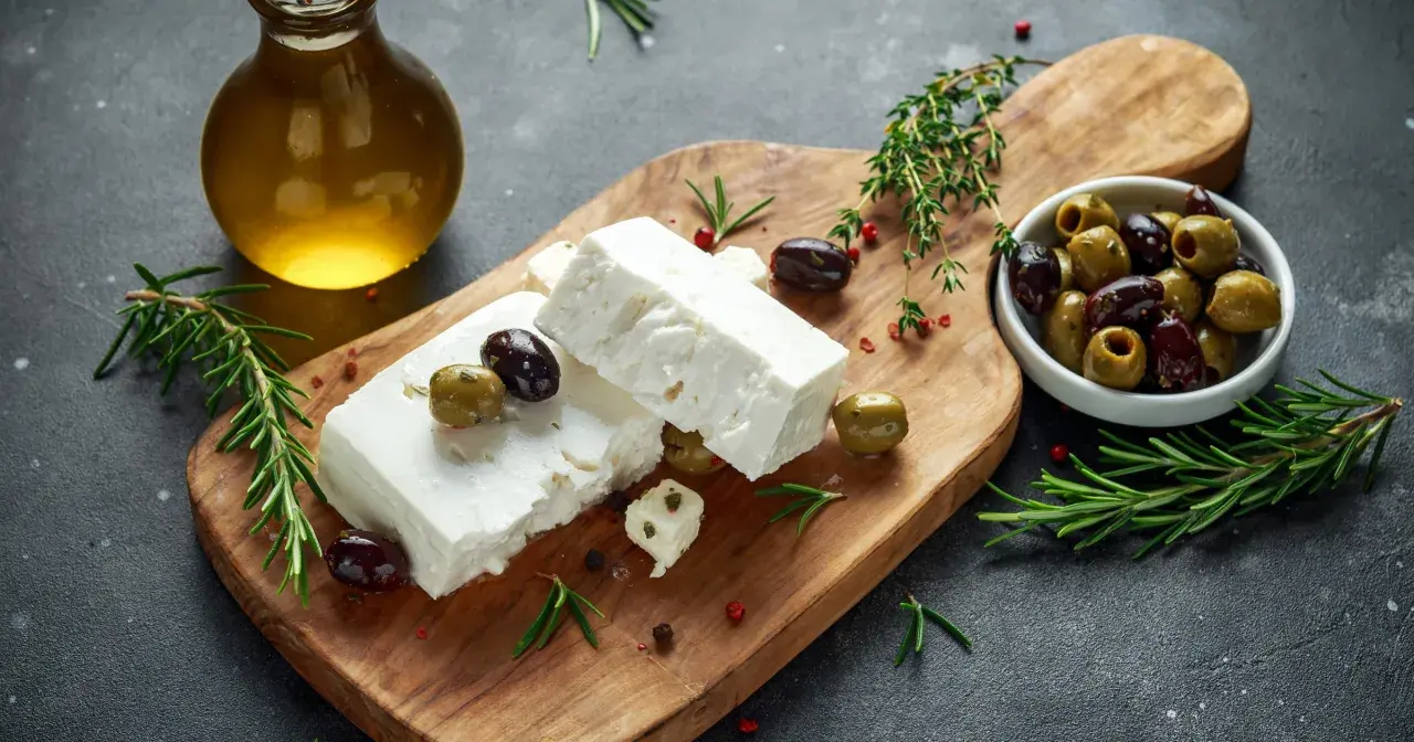 Ser feta na desce z oliwkami i rozmarynem. Warto sprawdzić ser feta kcal, by świadomie cieszyć się smakiem.
