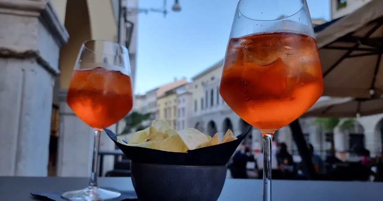 Dwa drinki Aperol Spritz i miseczka chipsów na stoliku. Czy alkohol podnosi cholesterol? To pytanie zadaje sobie wielu, popijając orzeźwiający drink.