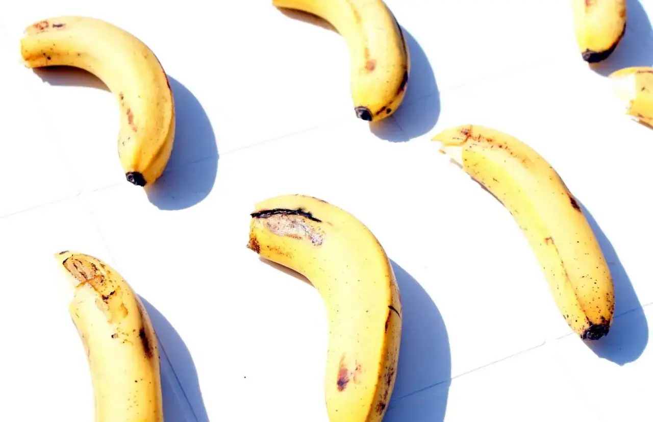 Kilka lekko zepsutych bananów, niektóre nadgryzione, leżących na białej powierzchni. Może to być pomocne przy zatruciu pokarmowym.