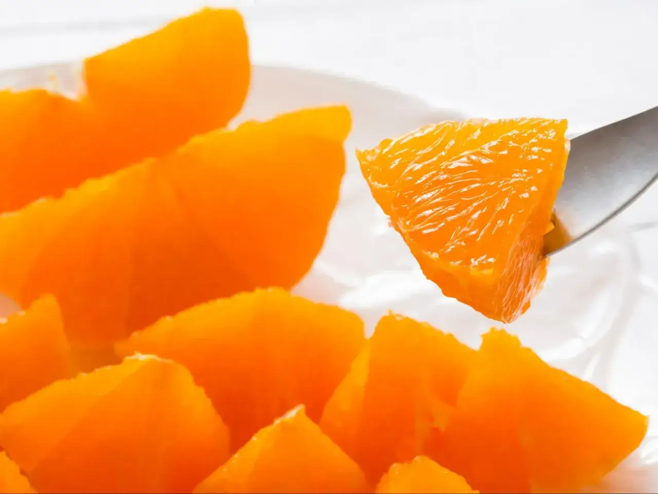 Kawałki soczystej pomarańczy na talerzu, jedna porcja na widelcu. Zdrowa przekąska, niska pomarańcza kcal.