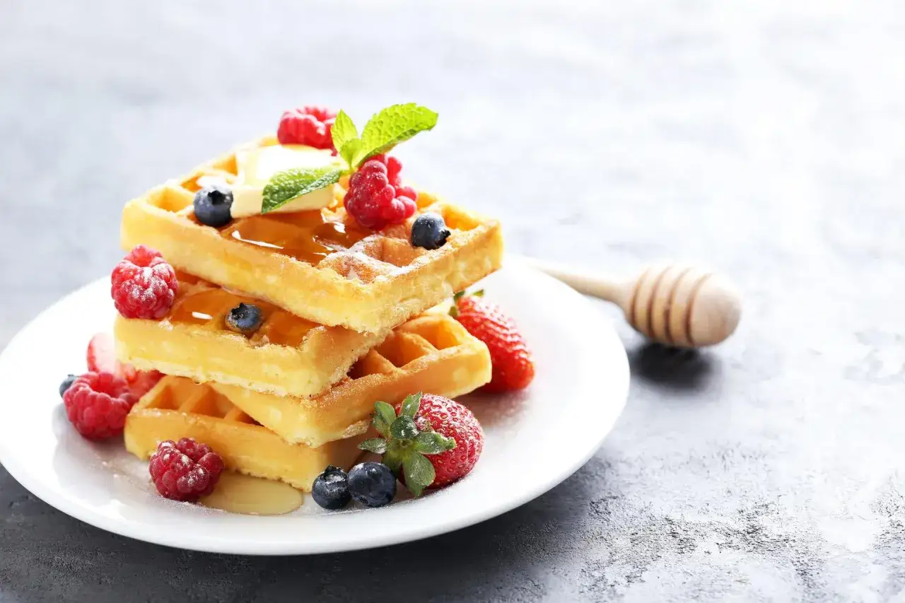 Stos gofrów z malinami, borówkami i miodem. Zastanawiasz się, ile kcal ma gofr? Ten wygląda pysznie!